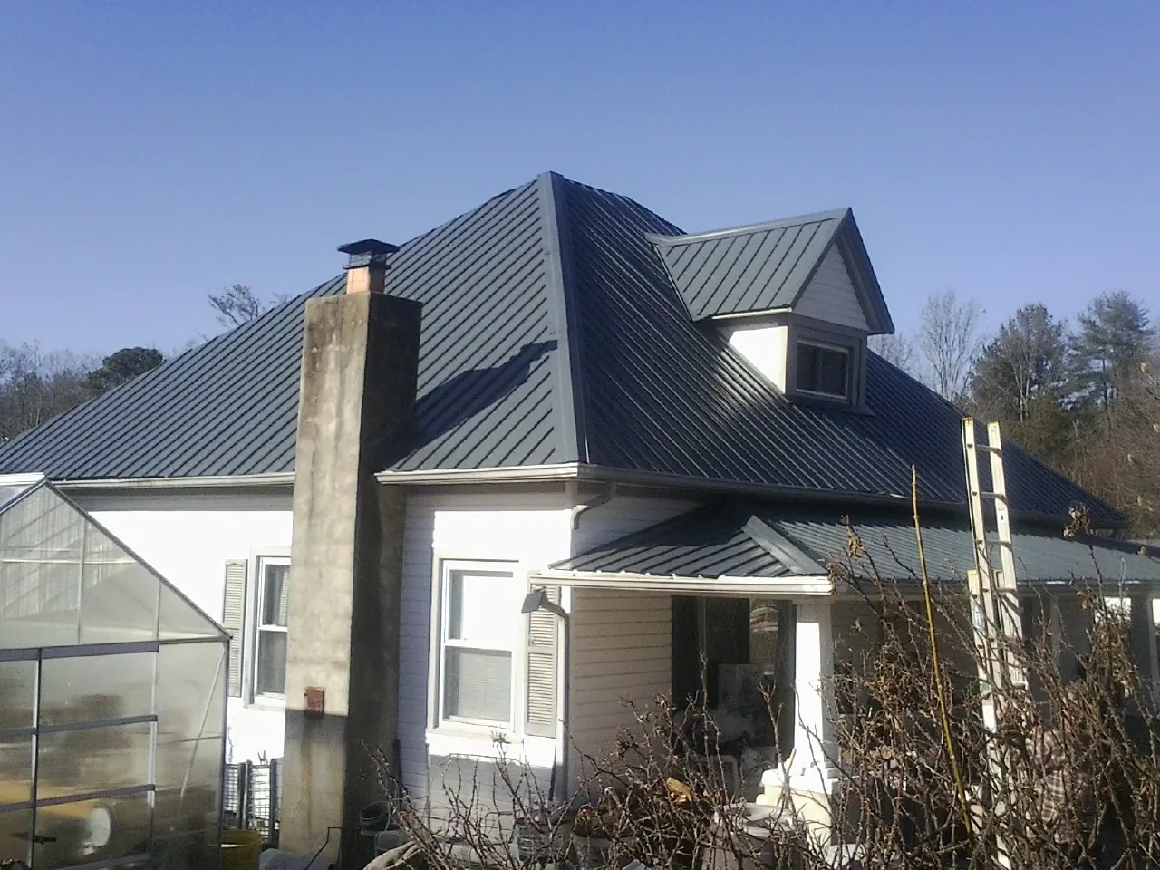 Dark blue standing seam metal roof on a white farmhouse with dormer — Slate & Tile Roof Repair by Roofing Brothers in Farley