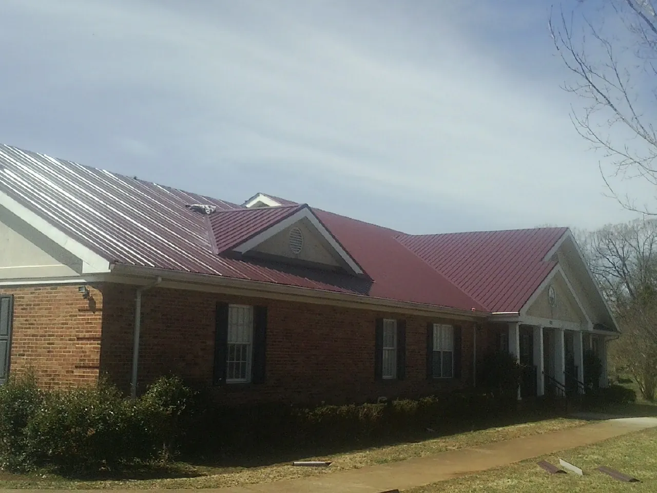 Red metal roof with gabled entries on a long brick building, from a Hail Damage Roof Repair job in Farley